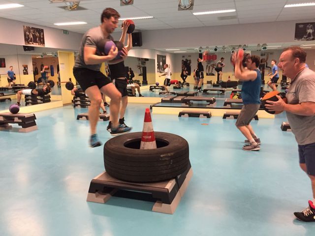 Mensen doen een workout in de sportschool met medicijnballen, banden en steps. Binnen in een sportschool met spiegels en apparatuur.