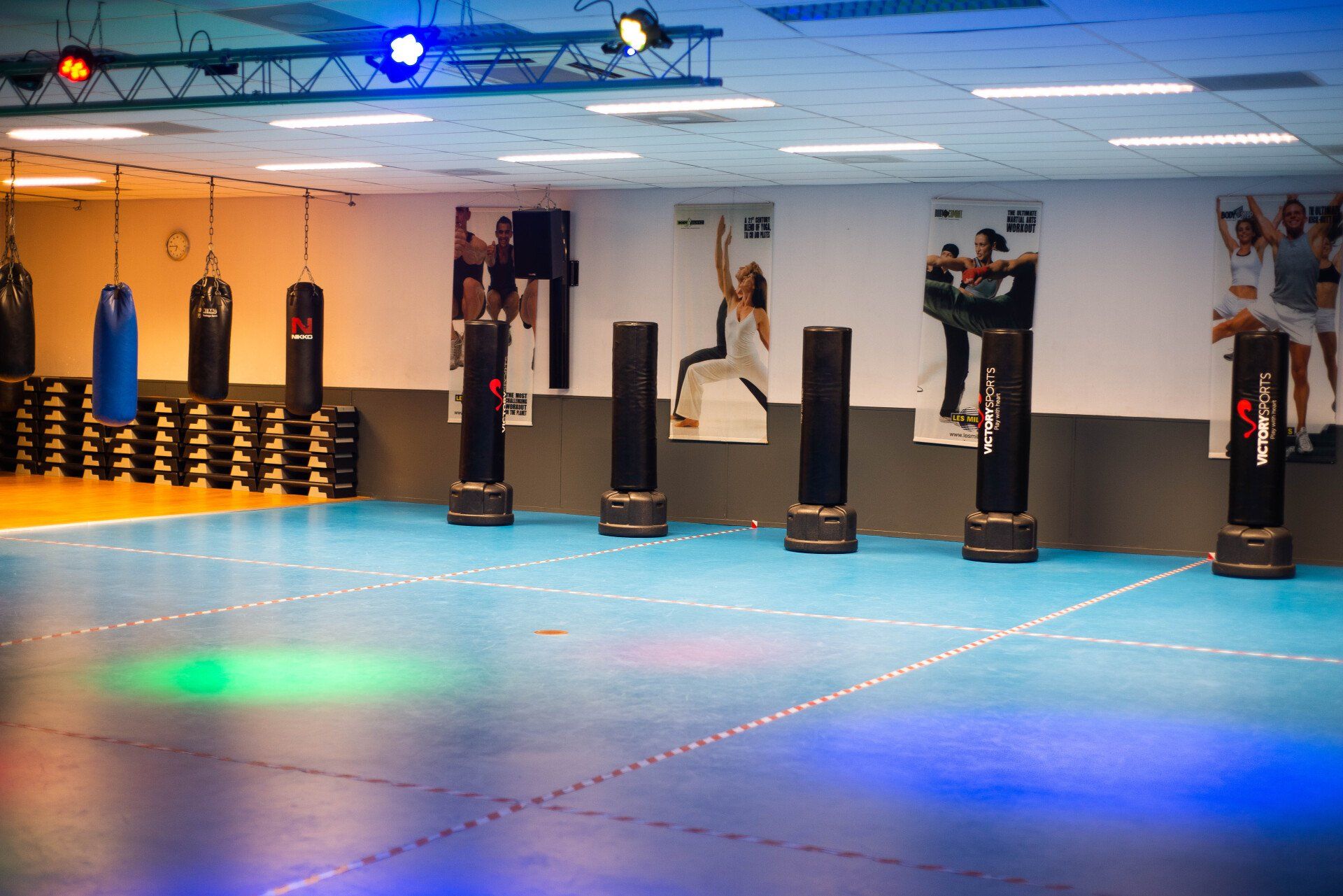 Interieur van een sportschool met bokszakken en bokstribunes op een blauw-oranje vloer.