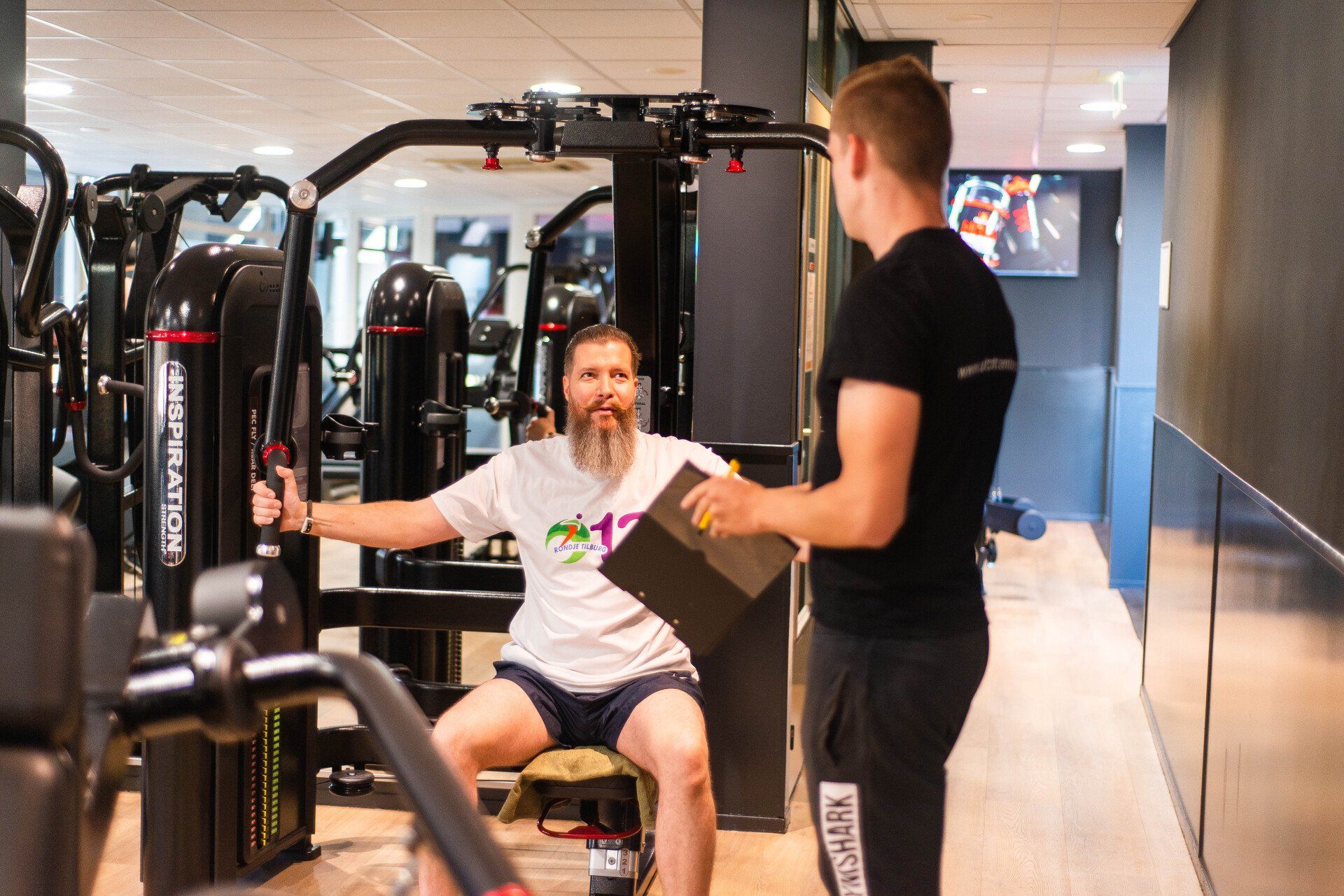 Een trainer helpt een man bij het bankdrukken van een halter in een sportschool.