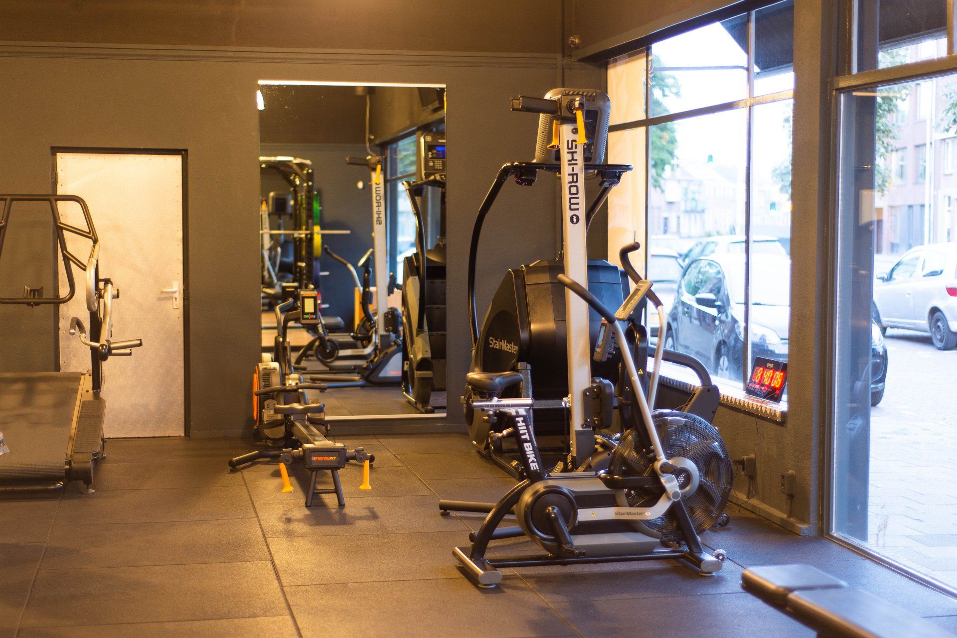 Fitnessruimte met fitnessapparatuur: loopband, luchtfietsen, roeimachine en spiegels.