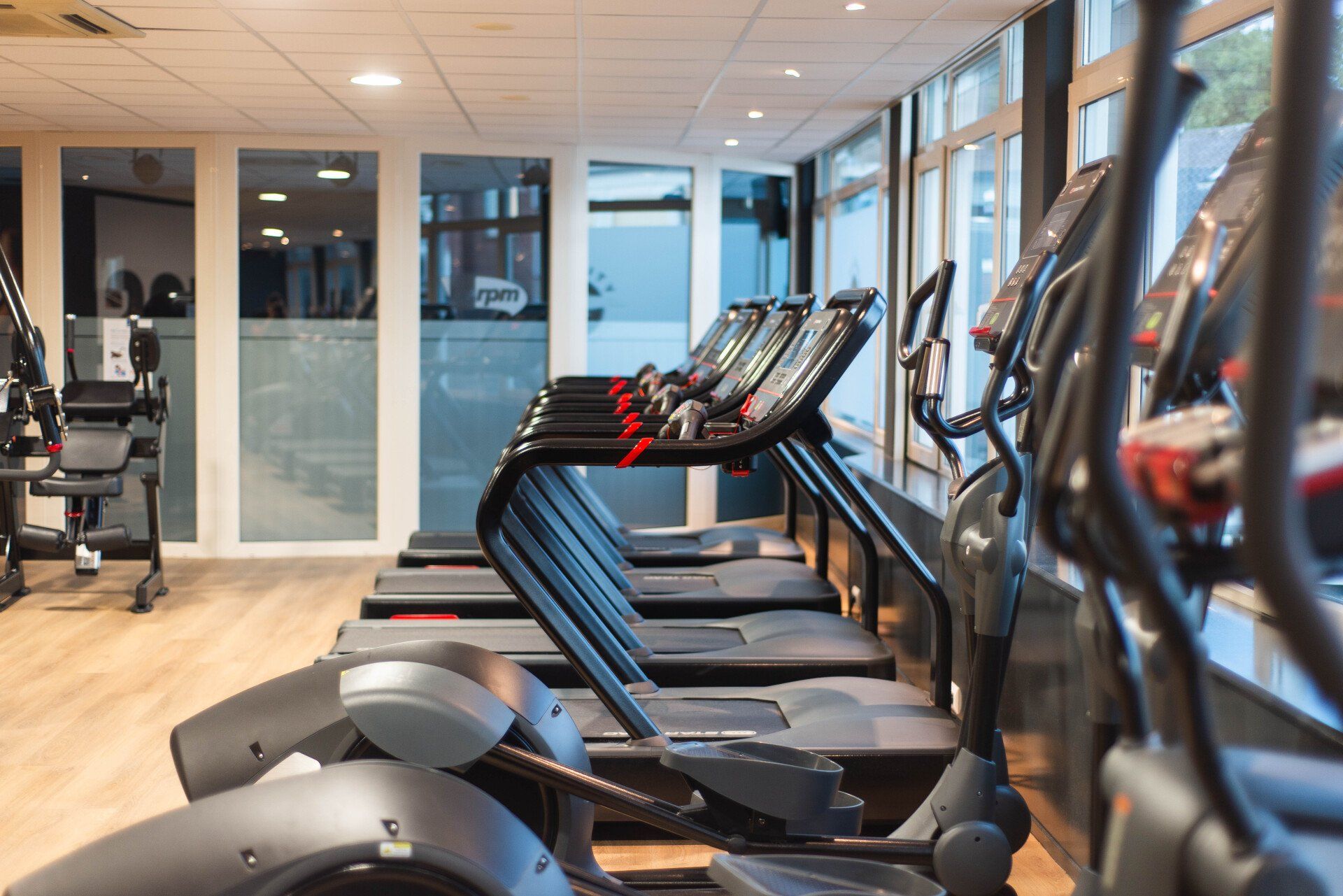 Een rij loopbanden en crosstrainers in een felverlichte sportschool.