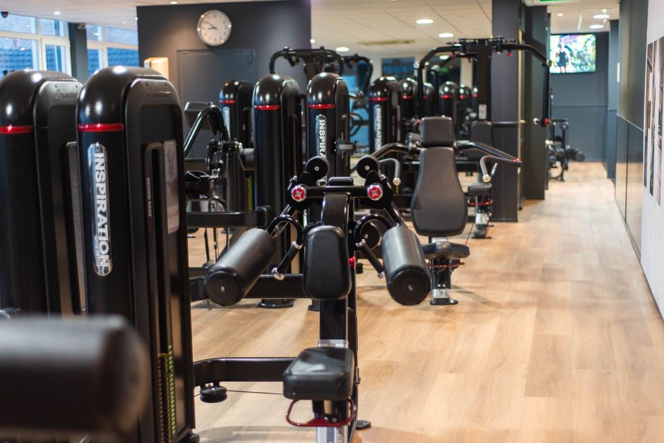 Interieur van een sportschool met zwarte gewichten, een houten vloer en een klok aan de muur.