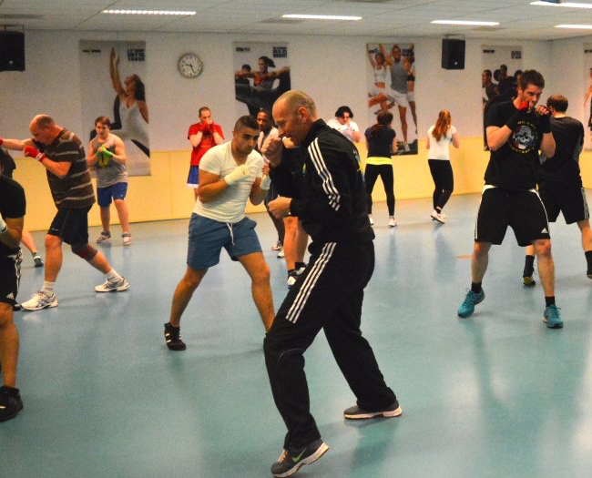 Boksles in een sportschool. De instructeur demonstreert stoten terwijl anderen oefenen.