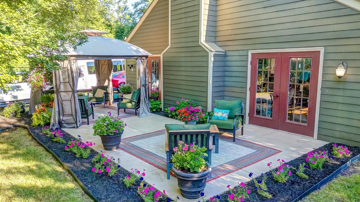 A large patio with a gazebo and flowers in front of a house.