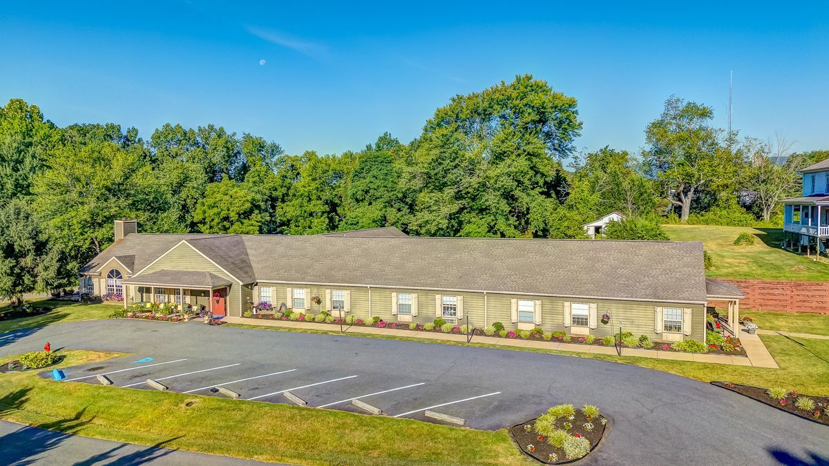 An aerial view of a large house with a parking lot in front of it surrounded by trees.