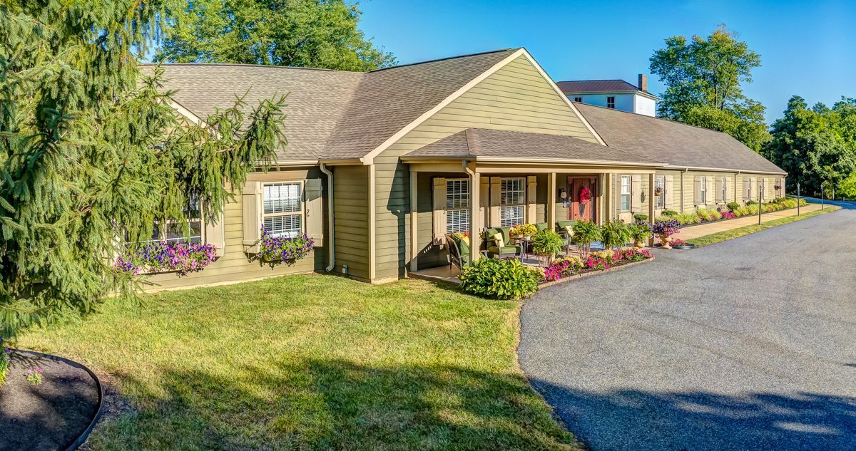 A large house with a large porch is sitting on top of a lush green field.