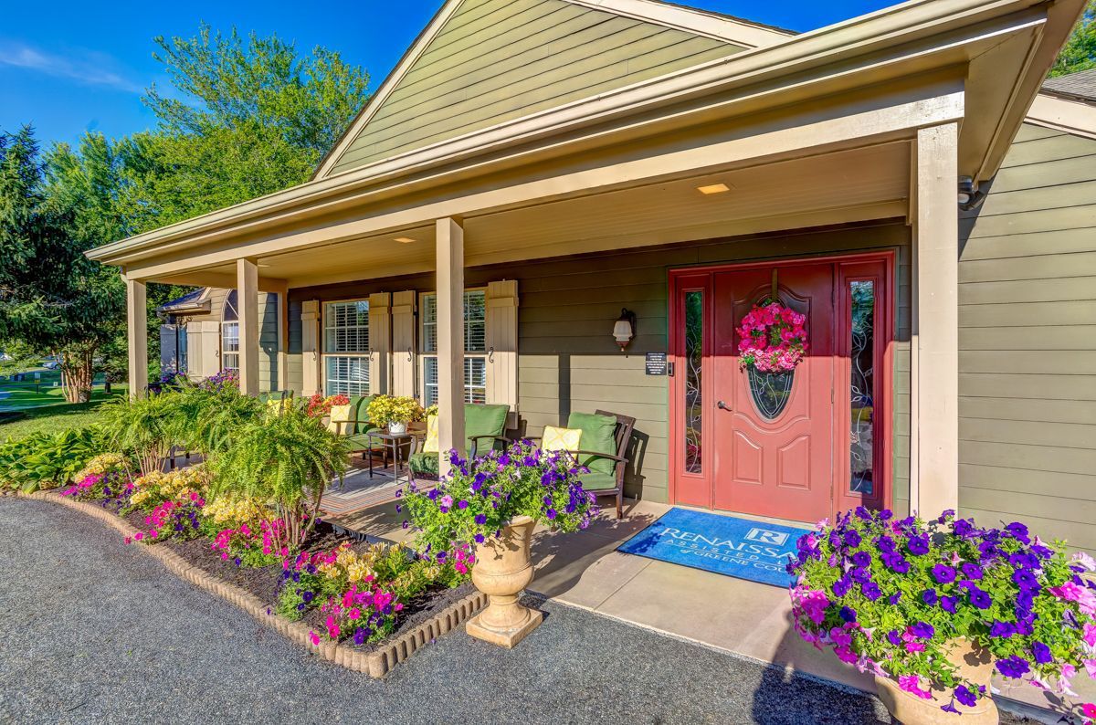 A house with a red door and a porch with flowers in front of it.