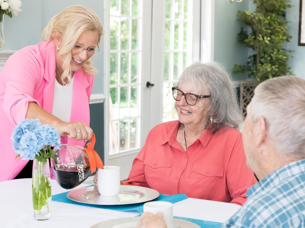 A woman is pouring wine into a cup for two elderly people sitting at a table.