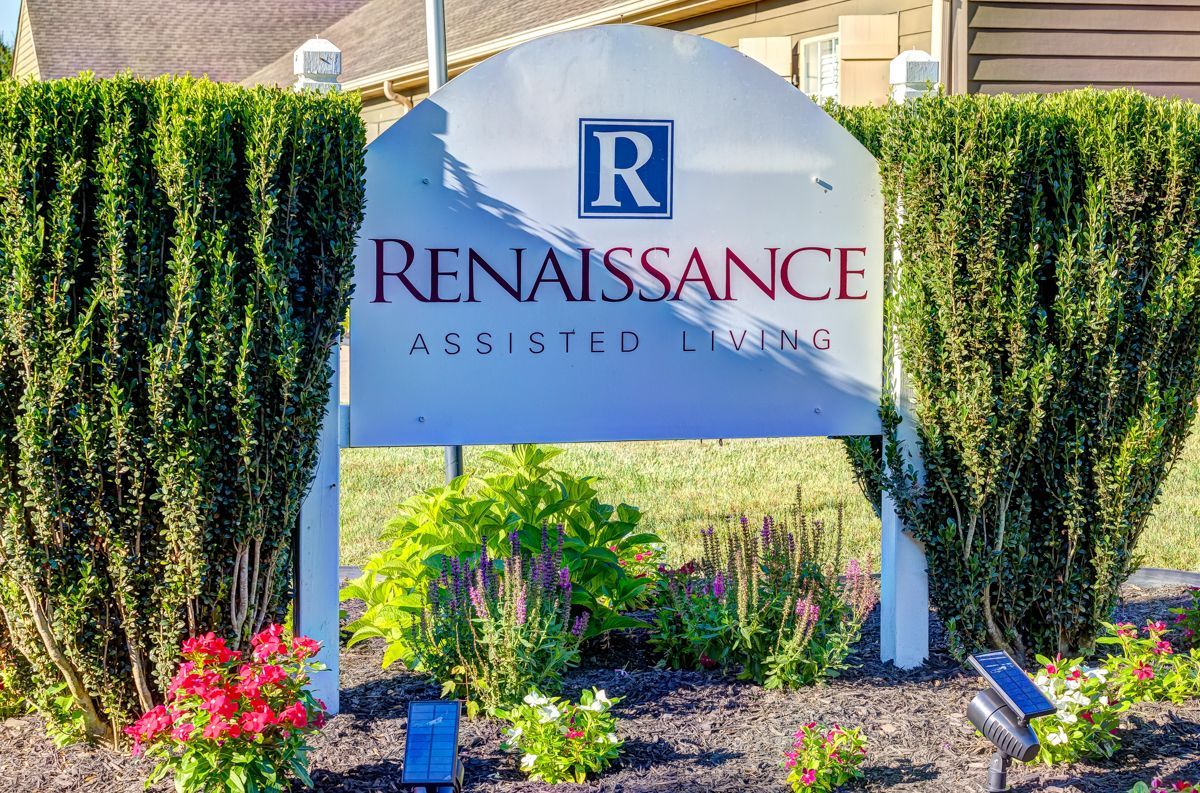 A sign for renaissance is surrounded by bushes and flowers