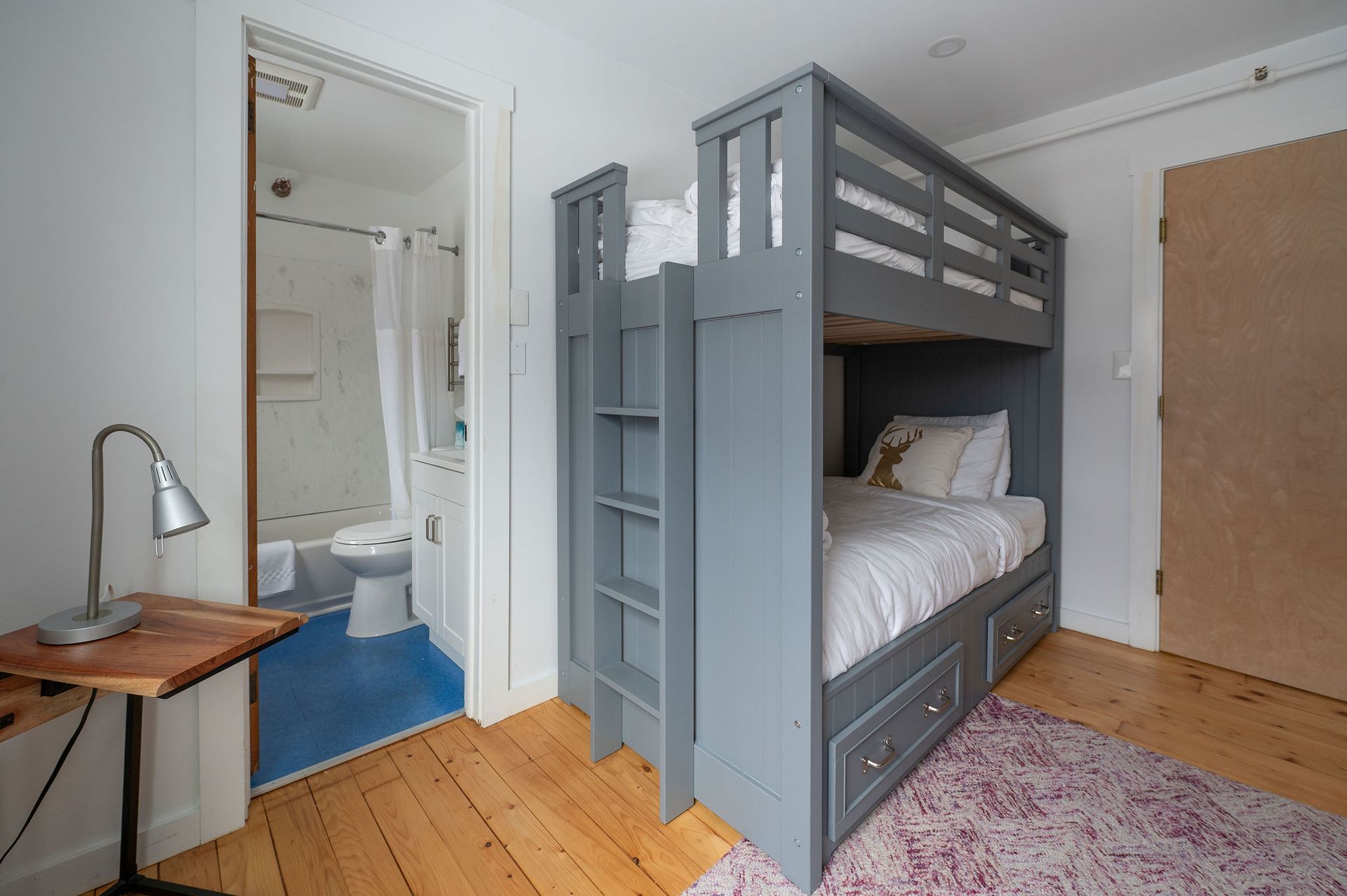 Gray bunk beds in a room, a bathroom visible through an open door, wooden floors and a small rug.