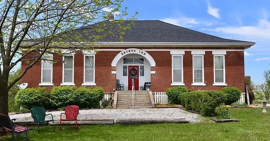 Brick building with white trim, a red door, and a sign that reads "Studio Law"; two chairs sit outside.