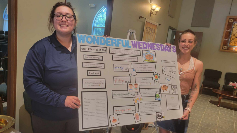 Two people holding a “Wonderful Wednesday” poster in a room, smiling at the camera.