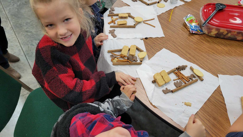 Children decorating gingerbread houses at a table, with frosting, candy, and smiling faces.