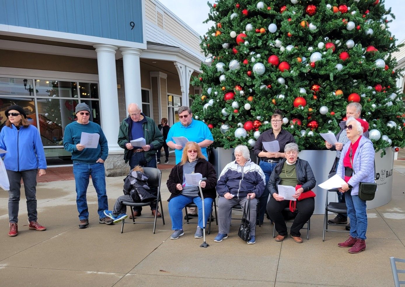 Group gathered beside a large decorated Christmas tree outside a building