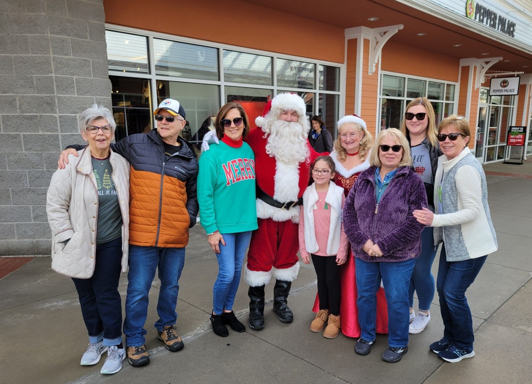 Group posing with Santa outside a brick storefront, smiling and dressed in winter clothes