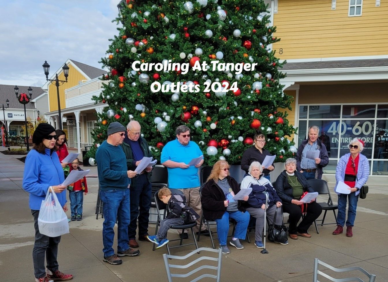 Carolers singing beside a decorated Christmas tree at Tanger Outlets 2024