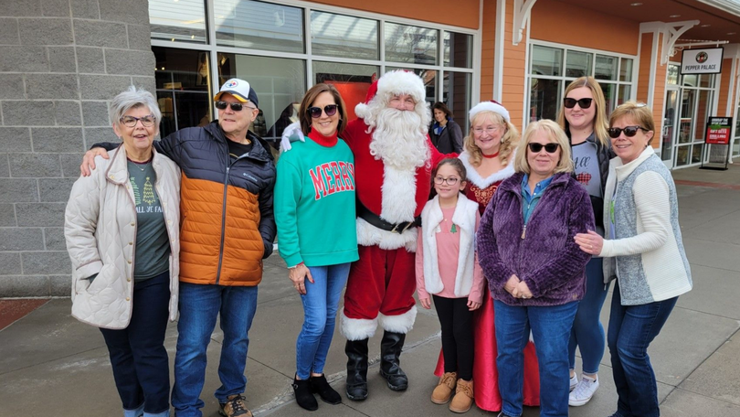 Group posing outside a storefront with Santa Claus, bundled in winter clothes and smiling