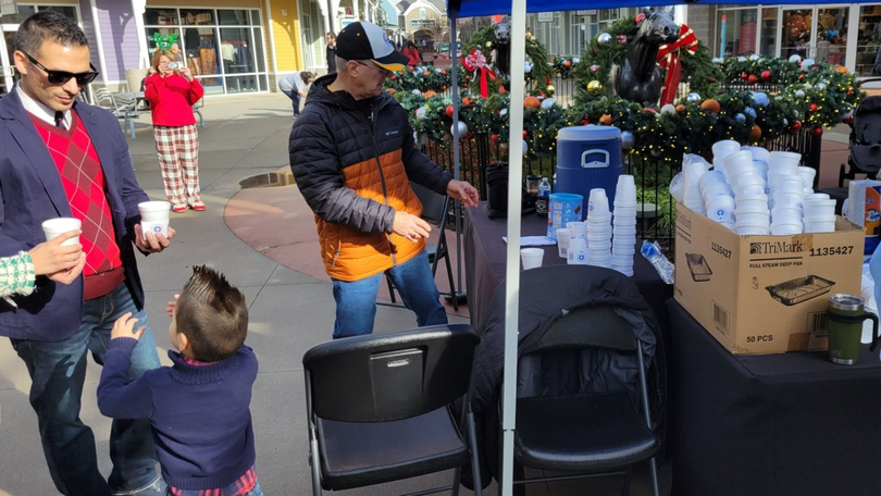 Musician playing guitar at a holiday charity table with drinks and decorations outdoors