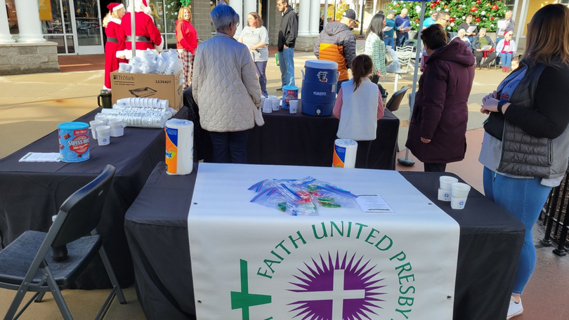 Outdoor church outreach table with black cloth and “Faith United Presbyterian” banner at a busy market.
