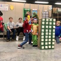 Children in costumes at a classroom party, with a green checkered tower in the foreground