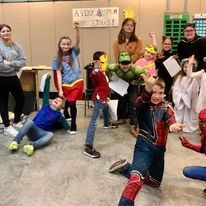 Group of children in colorful superhero costumes posing in a classroom with two adults.