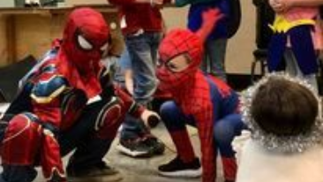 Two children in Spider-Man costumes crouch indoors, facing a small child in a furry hood.
