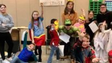 Children in colorful costumes posing in a classroom, smiling and holding props.