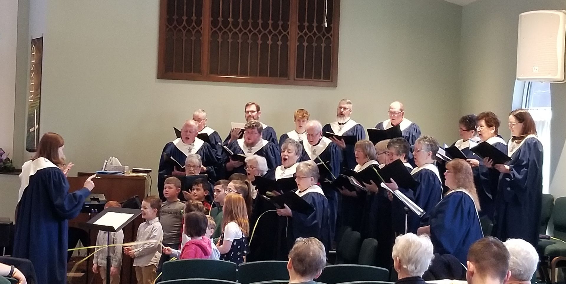 Choir singing in a church, led by a conductor, with a pianist in front