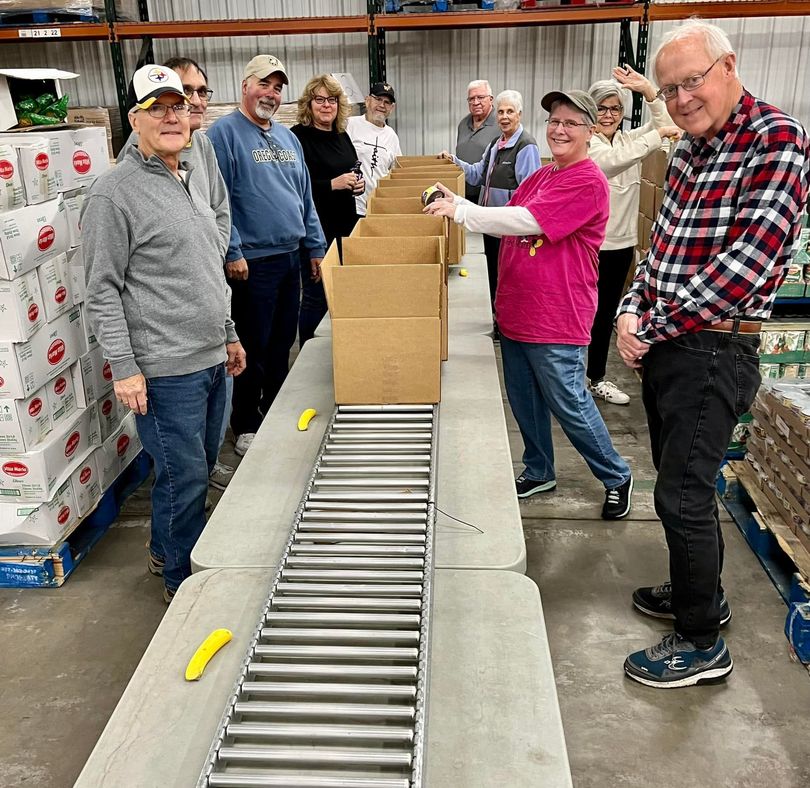 Volunteers stacking boxes beside a conveyor belt in a warehouse, smiling and working together