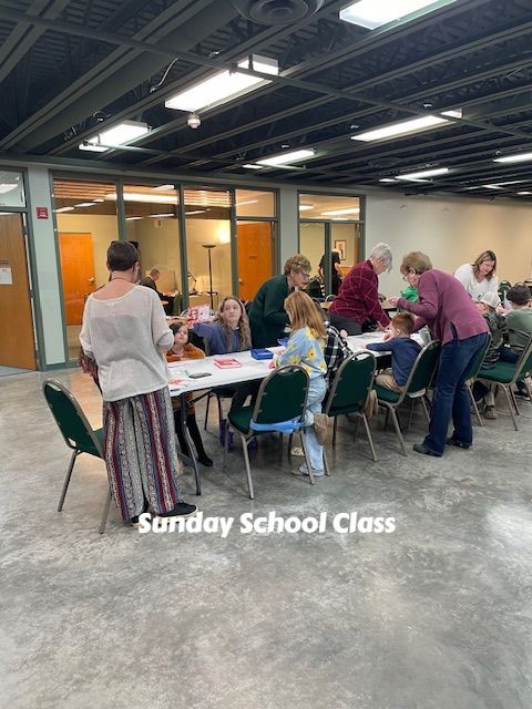 Sunday School class gathered around tables in a bright hall, chatting and working together