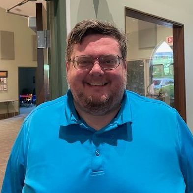 Smiling man in glasses wearing a bright blue polo shirt indoors.