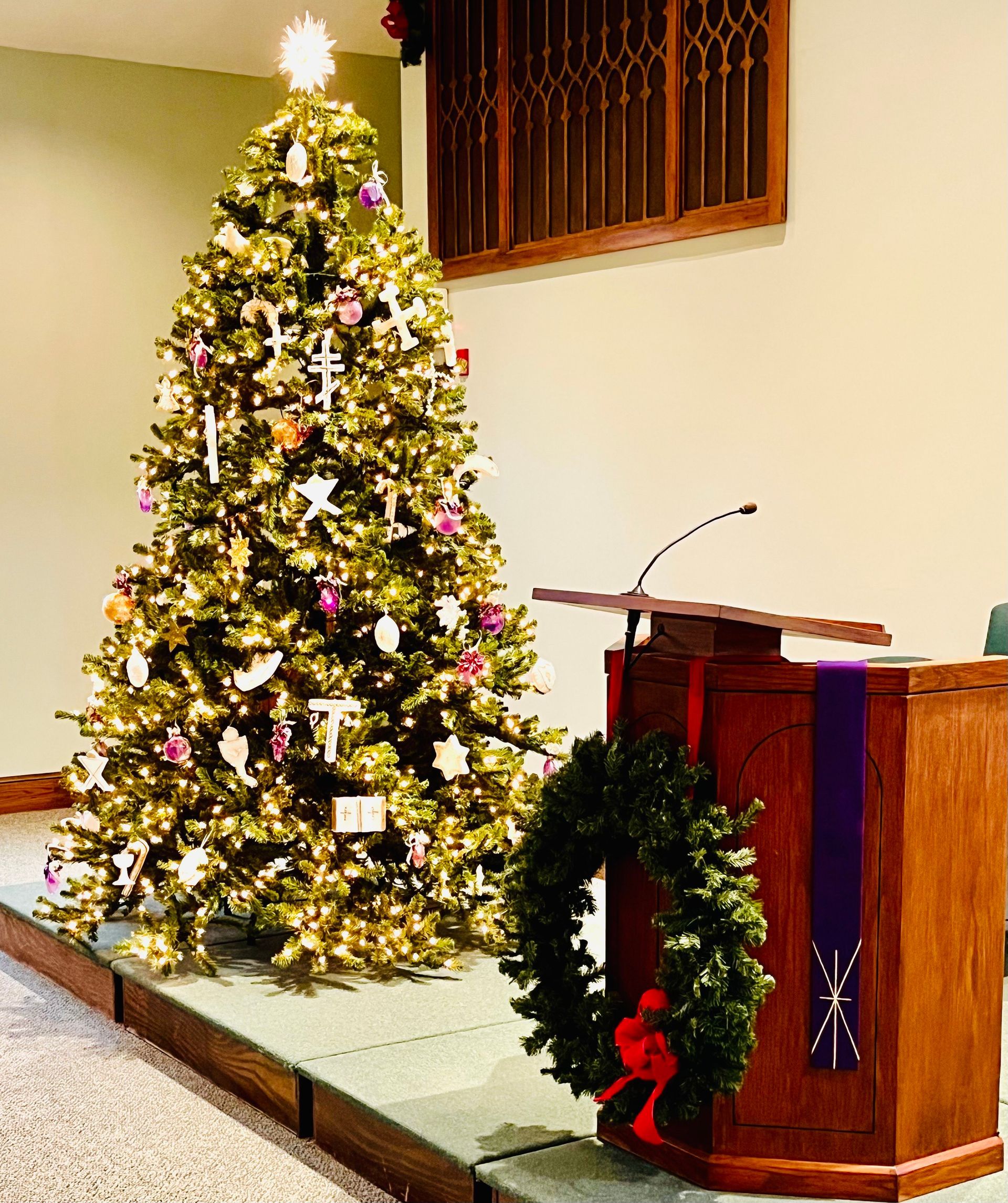 Decorated Christmas tree beside a church lectern draped with a green wreath and red bow