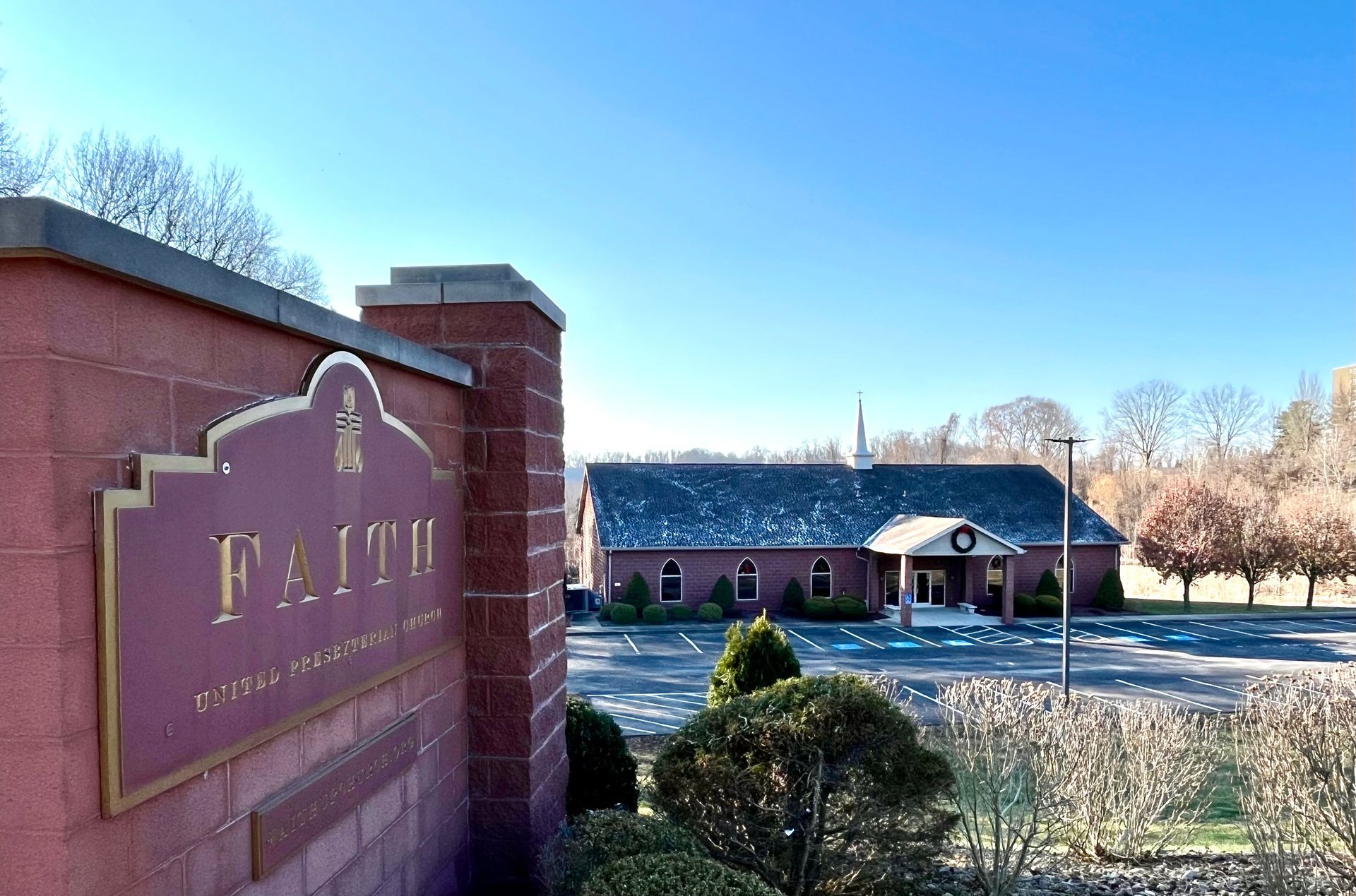 Brick campus entrance sign beside a red-brick building under a clear blue sky