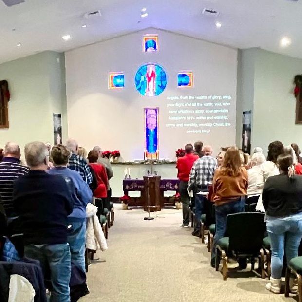 Congregation standing in a church sanctuary during a service, facing a lit stage and projected text.