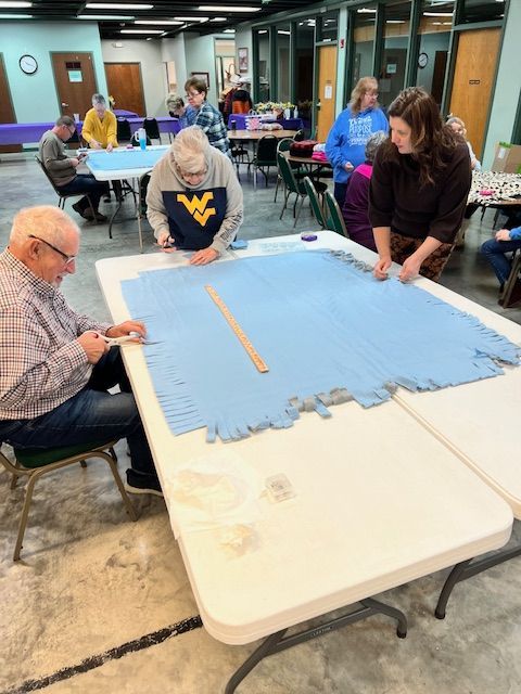 People gathered around a large blue fabric piece on tables in a workshop room.
