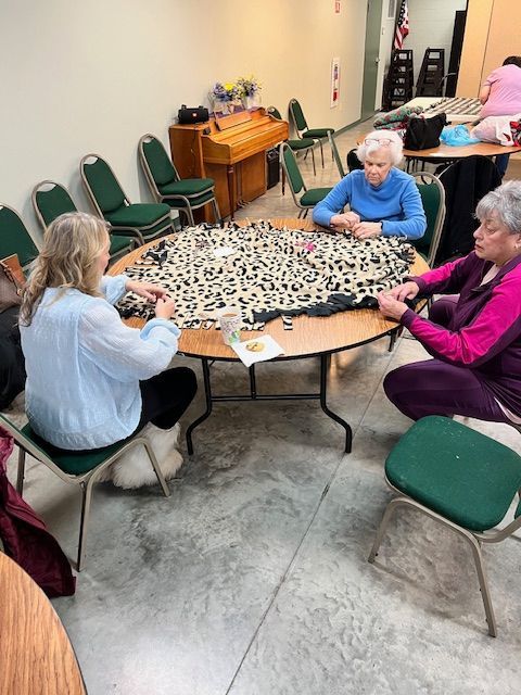 Four people sit around a round table in a community room, playing a board game on a leopard-print cloth.