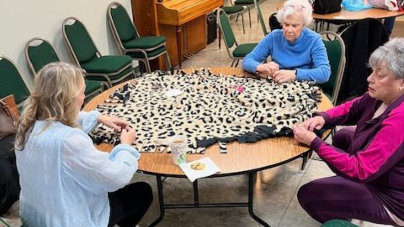 Three people sit around a table playing a spotted board game in a community room