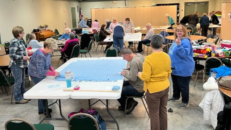 People gathered in a hall around tables with supplies, setting up or crafting at a community event.