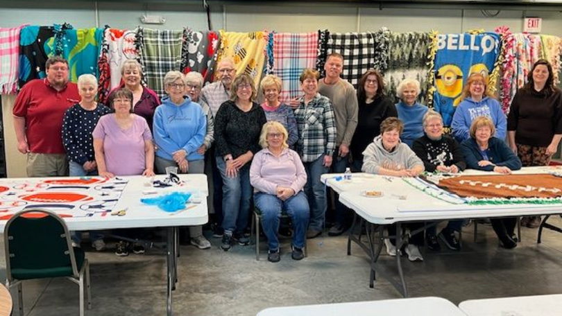 Group posing in a classroom with craft tables, colorful decorations, and a “WELCOME” banner behind them
