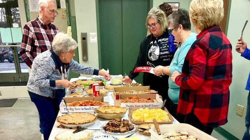 People serving themselves at a buffet table with trays of food in a bright indoor room