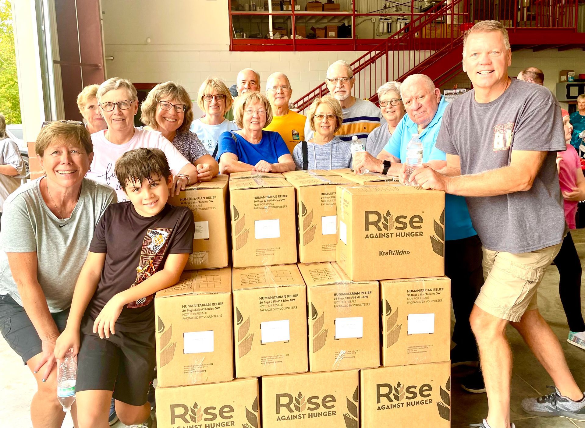 Group of volunteers smiling behind stacked Rise-branded boxes in a bright indoor room