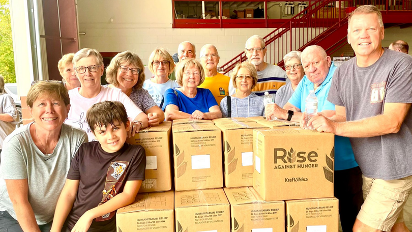 Volunteers posing with boxes of food donations in a bright indoor room