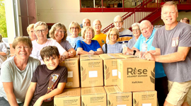 Volunteers gathered behind stacked boxes in a bright room, posing for a group photo.