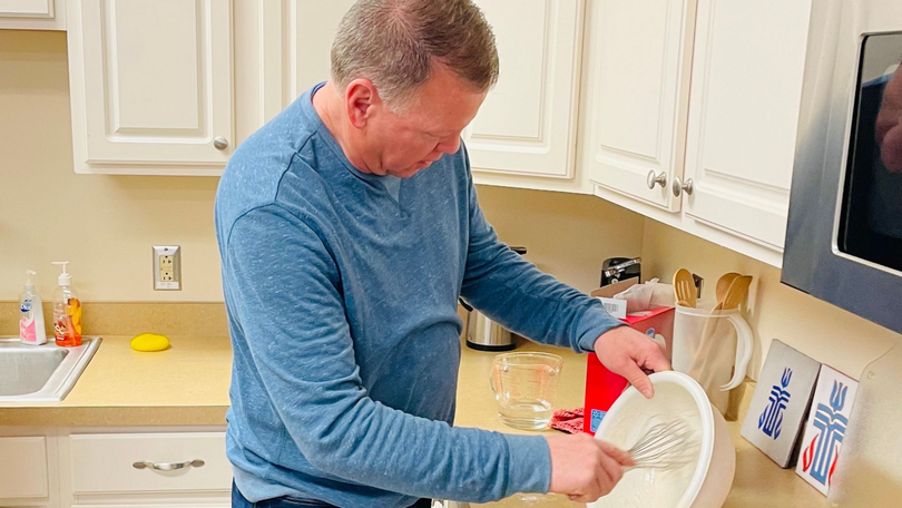 Man in blue shirt washing dishes in a kitchen beside a countertop and sink