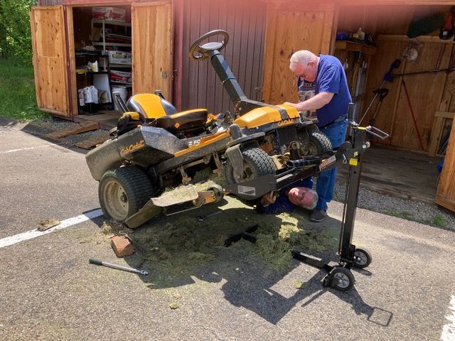 Mechanic repairing a yellow ATV on a driveway beside an open garage