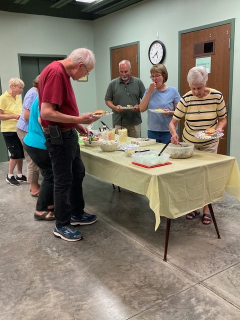 People standing around a table at an indoor gathering, serving food and drinks.