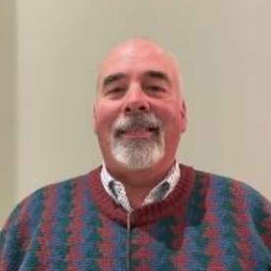 Smiling man in a red and teal patterned sweater against a plain wall