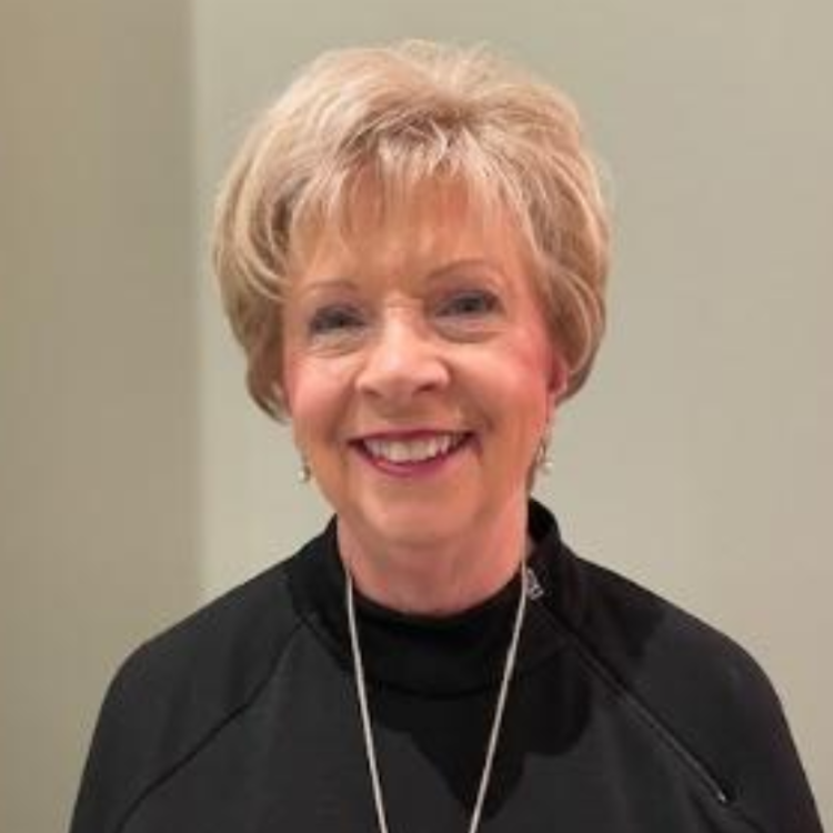 Smiling woman in a black top and silver necklace against a plain beige wall