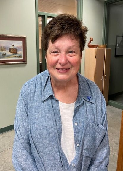 Smiling person in a blue shirt standing in an office hallway.