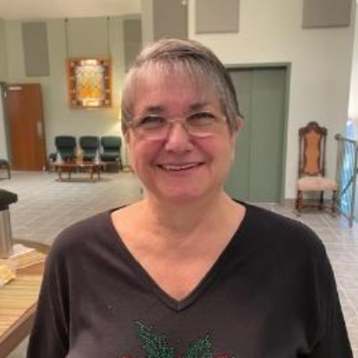 Smiling person in a dark shirt standing in a bright indoor room with chairs and wall art